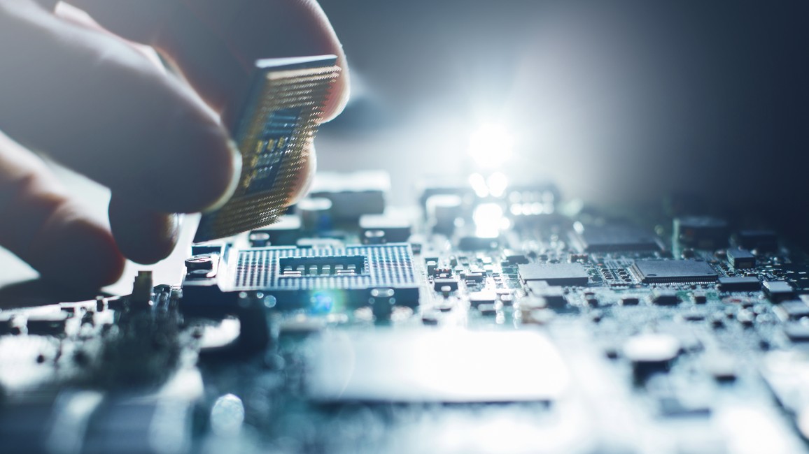 Eine Hand setzt einen Chip auf eine Platine ein.