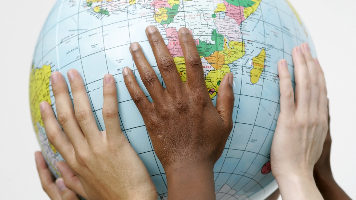 Hände von Menschen verschiedener Ethnien halten gemeinsam eine Weltkugel in die Höhe.